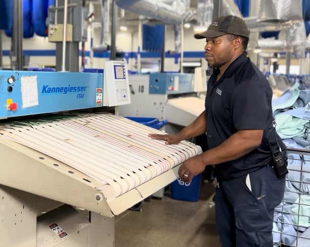 A male HHS team member utilizing advanced laundry automation technology to solve healthcare facility labor and equipment challenges