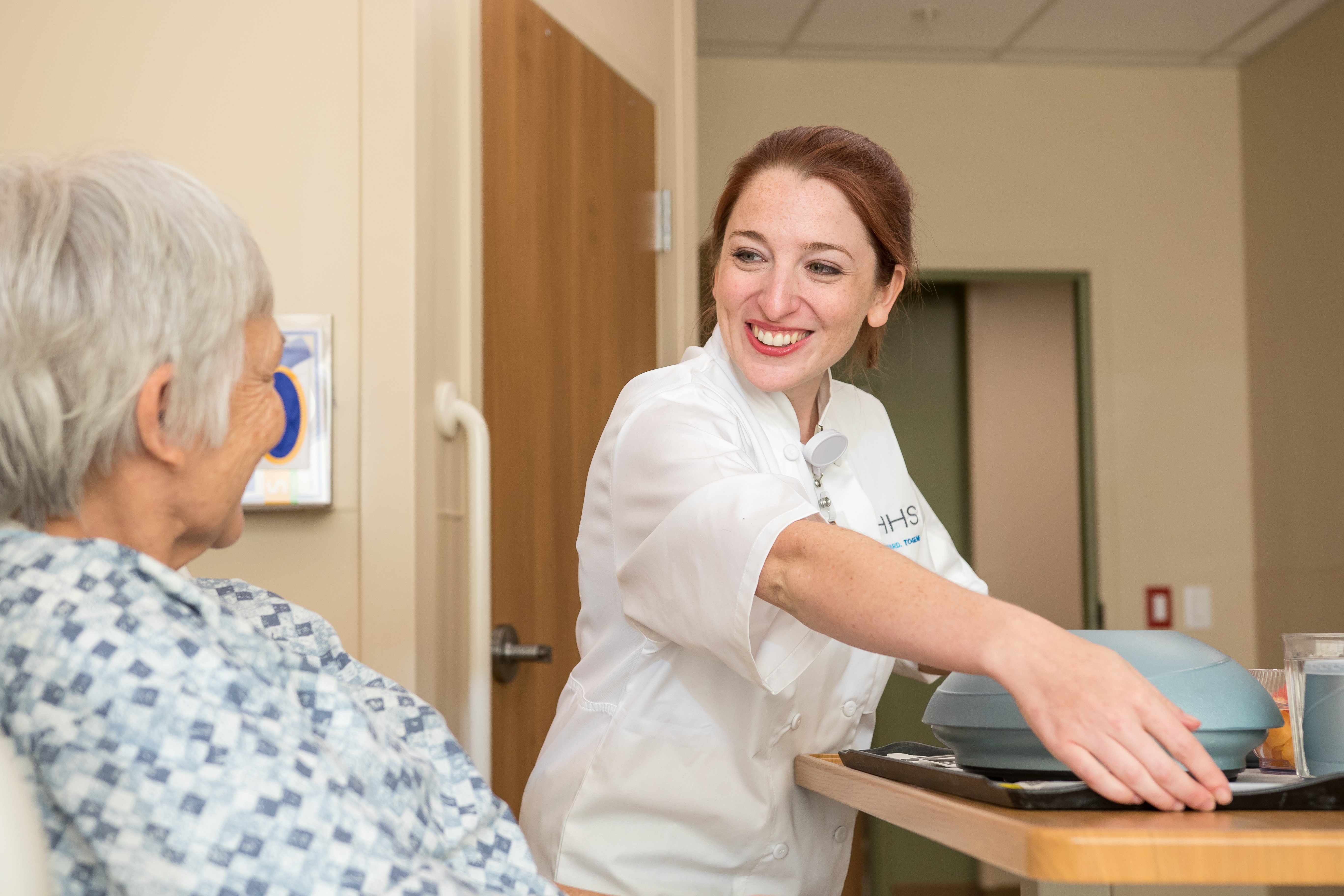 HHS Culinary team member delivers a meal to a hospital patient, demonstrating personalized care and support services.